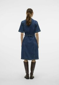 Denimklänning med korta ärmar, bälte i midjan och knälång längd. Har kontrasterande sömnad och kombineras med bruna stövlar som går till knäna.