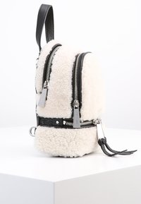 Kompakt ryggsäck med vitt fluffigt fårskinnsmaterial och svarta läderdetaljer. Har dubbla dragkedjefickor och silverfärgade detaljer.