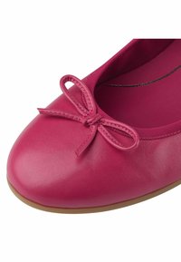 Gros plan d'une ballerine rose avec un nœud cousu sur l'avant arrondi et une semelle lisse marron.