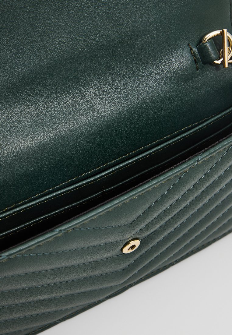 Intérieur d'un sac à main en cuir vert avec texture matelassée, accessoires en or et fermoir à pression. Dispose d'un compartiment divisé pour l'organisation.