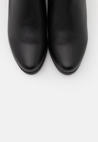 Bottes à cheville en cuir noir avec une texture lisse, un bout arrondi et un design minimaliste. Aucun élément métallique visible ni motif.