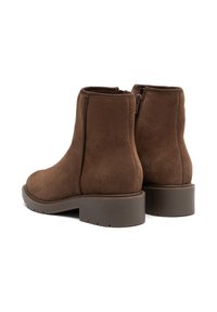 Par de botas de ante marrón hasta el tobillo con cremalleras laterales y tacones bajos y gruesos, vistas desde la parte trasera y lateral sobre un fondo blanco.