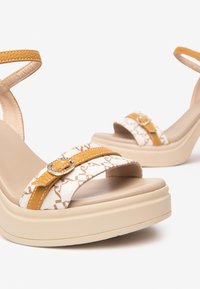 Sandali platform bianchi e beige con una parte superiore testurizzata, una cinghia gialla con dettaglio a fibbia tondeggiante e un tacco grosso beige.