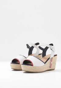 Vita wedge-sandaler med öppen tå-design, vävd juteplattform, marinblå detaljer och justerbara ankelsnoddar. Slät läderöverdel.