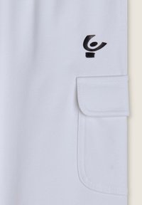 Pantaloni cargo bianchi realizzati in tessuto morbido, con una tasca a patta e un piccolo dettaglio con logo nero sul davanti. La cucitura è visibile lungo i bordi.