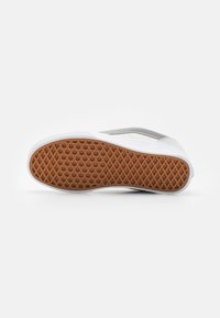 Weißer Sneaker mit glattem Obermaterial, grauen Akzenten und einer strukturierten Gummisohle in einem Rautenmuster. Die Sohle ist braun mit einem Waffelmuster.