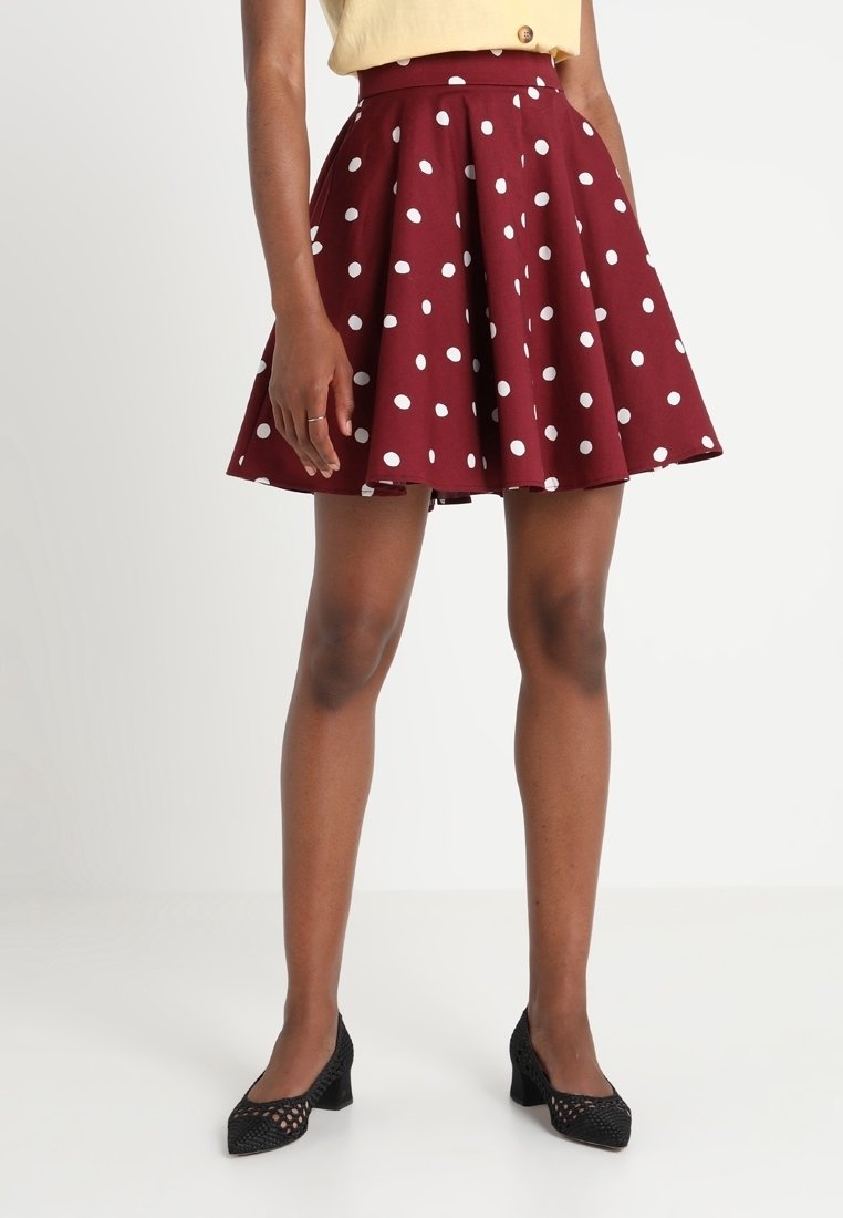 Mörkröd kjol med vita prickar, A-linjeformad design, knälång, gjord av ett tyg med en mjuk textur. Bärs med svarta låga klackskor.