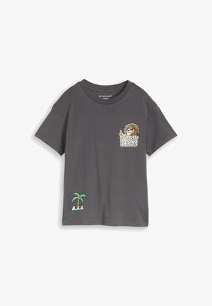T-shirt oversize gris foncé avec un lion caricatural portant des lunettes de soleil et le texte « Vacation Team » sur la poitrine, ainsi qu'un palmier avec des vagues en bas.