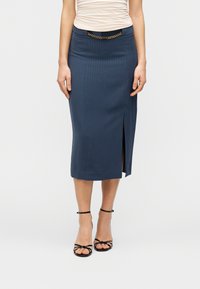 Εξατομικευμένη μολυβοειδής φούστα σε ναυτικό μπλε με κάθετες λεπτές ρίγες, πλάγια σκίσιμο και μαύρη ζώνη μέσης με χρυσή λεπτομέρεια αλυσίδας. Συνδυασμένη με μαύρα πέδιλα με λεπτά λουράκια.