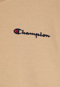T-shirt in cotone beige con logo "Champion" ricamato in blu scuro, arricchito da un accento rosso e blu all'interno della lettera "C."
