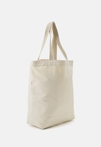 Beżowa torba na zakupy z bawełny z dwoma materiałowymi uchwytami, prostokątny kształt, gładka powierzchnia, wzmocnione szwy w miejscach łączenia.