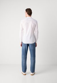 White long-sleeve shirt with a collar, paired with light blue denim jeans. White sneakers with a tan sole are worn. Simple design and fit.