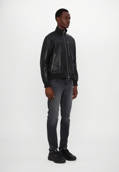 Μαύρο δερμάτινο μπόμπερ μπουφάν με ψηλό γιακά, διακοσμημένο με ασημένιες φερμουάρ και ελαστική μέση. Φοριέται με γκρι τζιν και μαύρα πάνινα παπούτσια.