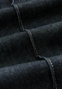 Tume denim kangas kergelt tekstureeritud pinnaga, millel on nähtavad kontrastse heleda värvi õmblused, volditud sügavuse ja detailide näitamiseks.