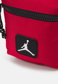 Borsa di tessuto rossa con superficie testurizzata, dotata di una cerniera nera e di una patch nera con il logo Jumpman bianco sul davanti.
