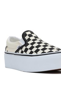 Zapato de lona a rayas en blanco y negro con suela blanca gruesa y costuras en negro. Presenta una etiqueta de Vans en el lateral.