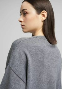 Maglione grigio lavorato a maglia con vestibilità ampia, scollo rotondo e spalle scese. Texture morbida con dettagli di cuciture minime.