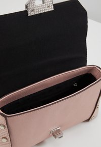 Růžová kožená kabelka s texturovaným povrchem, černým interiérem a stříbrným kovovým zapínáním. Obsahuje vnitřní zipovou kapsu.