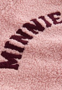 Gros plan d'un tissu rose texturé avec des lettres cousues en violet foncé formant un mot incurvé.