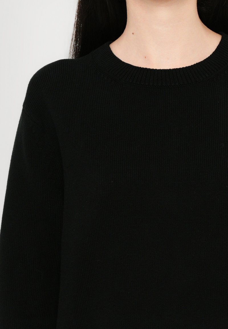 Black knitted sweater with a round neckline, featuring a ribbed texture and long sleeves, displaying a smooth finish and minimal detailing.