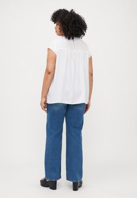 White short-sleeve blouse with a keyhole back, paired with light blue wide-leg jeans. Features a relaxed fit and soft fabric.