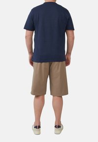 Marineblaues T-Shirt mit kurzen Ärmeln und Rundhalsausschnitt, kombiniert mit beigen knielangen Shorts und lässigen Schuhen mit einem schwarz-weißen Design.