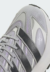 Gray and white athletic shoe featuring textured materials, reflective silver stripes, gray laces, and a "water repellent" label on the side.