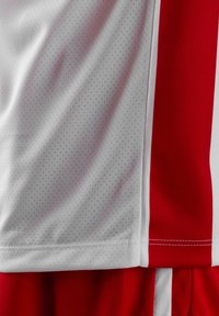 Maglia sportiva rossa e bianca caratterizzata da una texture in mesh traspirante, con pannelli laterali rossi solidi e cuciture a contrasto lungo l'orlo.