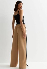 Pantaloni beige a gamba larga con strisce laterali nere, dotati di una vita elastica. Abbinati a un top aderente nero. Tessuto morbido.