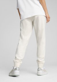 Pantaloni sudati beige chiaro con polsini elasticizzati e una texture liscia, abbinati a scarpe da ginnastica bianche e pastello con suola chunky.