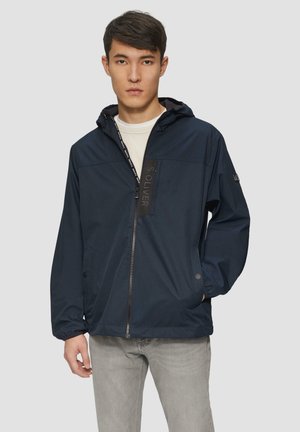 Marineblaue Windjacke mit einem Frontreißverschluss, verstellbarem Kapuzenrand und Logopatch. Verfügt über Seitentaschen und elastische Bündchen.