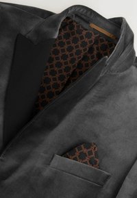 K charcoalgrauer Blazer aus weichem Stoff mit schwarzen Revers. Innenausstattung mit schwarzer Fütterung und geometrischem Muster in Braun sowie einem Einstecktuch.