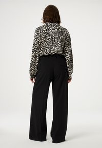 Black high-waisted trousers paired with a long-sleeve, cream blouse featuring a black abstract pattern. Blouse has a pleated back detail.