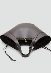 Bolso tipo saco de cuero marrón oscuro con correas ajustables, herrajes dorados y cierre de cordón, descansando sobre un fondo claro.