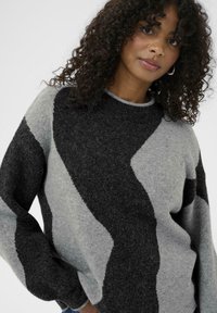 Sweater made of soft knit fabric featuring a wavy pattern in shades of grey and black, with a round neckline and long, loose sleeves.
