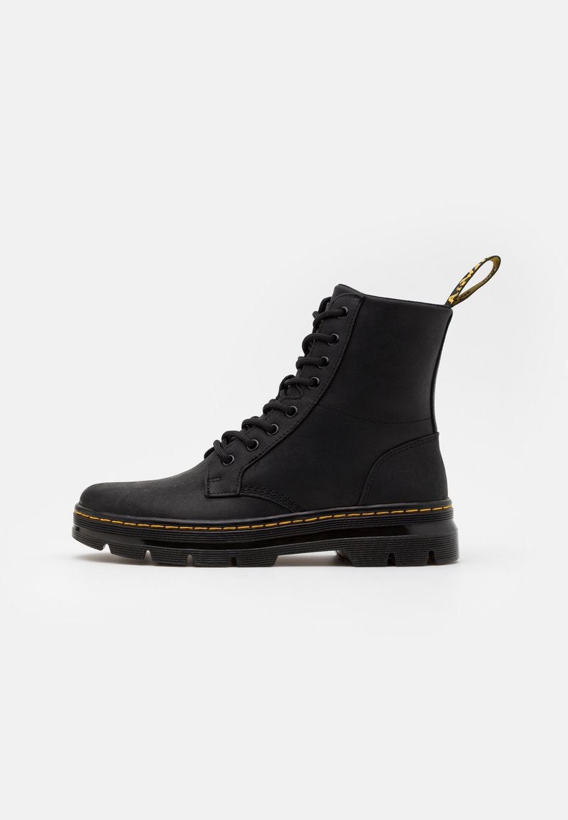 Botte en cuir noir à lacets avec semelle en caoutchouc épaisse, détail de couture jaune et boucle en tissu au talon sur fond blanc.