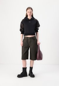 Μαύρη κοντή μπλούζα με διαφανή μανίκια, ελαιόκανα σορτς, μαύρα μποτάκια με κορδόνια και μπορντώ τσάντα χειρός. Απλά μοντέρνα σχεδιαστικά στοιχεία.