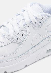 Baskets blanches avec tige en cuir, détails texturés, languette en mesh rembourrée et lacets plats. Présente un amorti à air et un logo signature.
