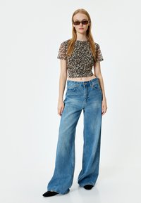 Top w panterkę z krojem cropped w przezroczystym materiale, zestawiony z szerokimi niebieskimi dżinsami. Gładka faktura; luźny krój z wysokim stanem i pięcioma kieszeniami.