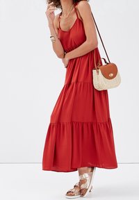 Robe maxi rouge avec une jupe à volants en tissu léger. Associée à des sandales métalliques et un sac bandoulière tressé.