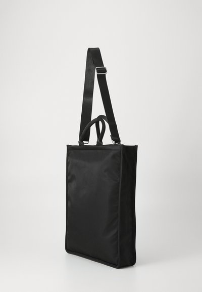 Black tote bag made from nylon with a rectangular shape, adjustable strap, and dual top handles. Smooth texture and no visible hardware.