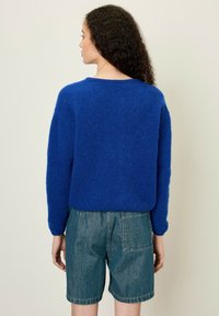 Blauwe pluizige trui met eenRelaxed fit, ronde hals en lange mouwen, gecombineerd met licht denim shorts met achterzakken.