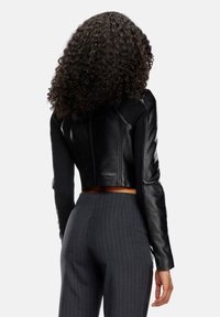 Veste en cuir noir coupée avec des manches en tissu côtelé, présentant un design ajusté et des détails de couture subtils. Associée à un pantalon rayé sombre.