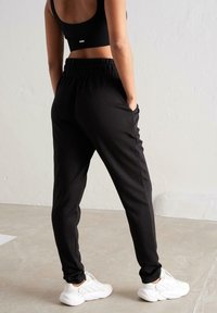 Sorte joggingbukser med elastisk talje, sidelommer og tapered ben, parret med hvide sneakers. Blød, glat tekstur.