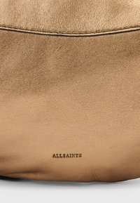 Tan læder skuldertaske med en glat tekstur, diskrete sydetaljer og prægede "ALLSAINTS" logo på siden. Rund form.