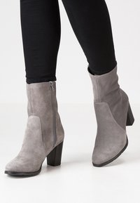 Botas de tobillo de ante gris con tacón cuadrado, que cuentan con un zipper lateral y un diseño de punta afilada. Material texturizado y líneas limpias.