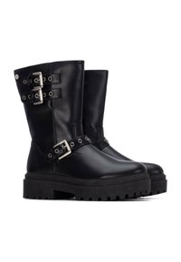 Botines de cuero negro hasta el tobillo con dos correas ajustables de hebilla plateada, suela gruesa y texturizada, y puntera redondeada. Presentan suelas de goma planas y costuras laterales.