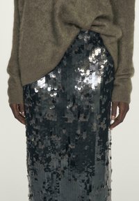 Person wearing a fuzzy brown sweater partially tucked into a high-waisted black sequin skirt, hands relaxed at sides.