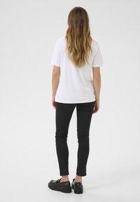 T-shirt blanche à manches courtes, jean slim noir et chaussures à plateforme noires, vues de dos. Tissu doux, design décontracté et style ajusté.