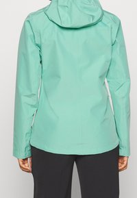 Ljus teal vattentät jacka med huva, figursydd design och långa ärmar. Har en slät, matt yta och minimalistisk stil.